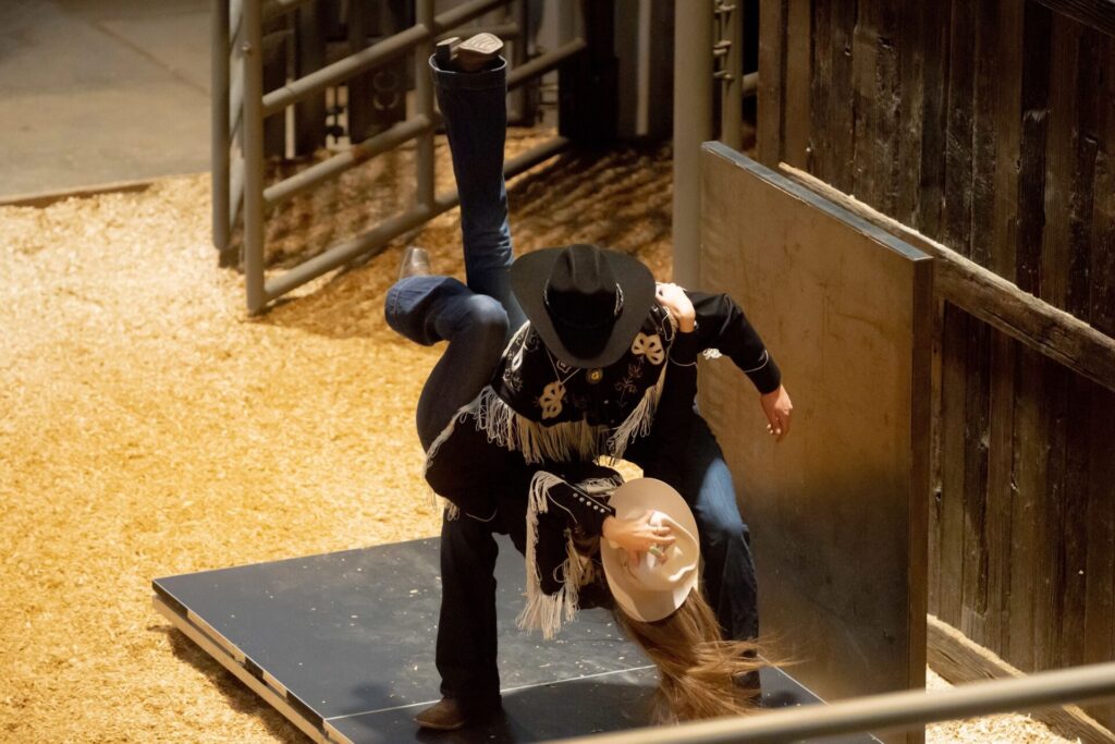 Two people in western wear dance on a stage.