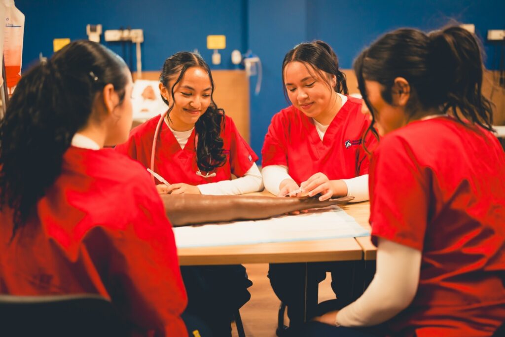 Four students in red scrubs gather around a table with a prosthetic arm.